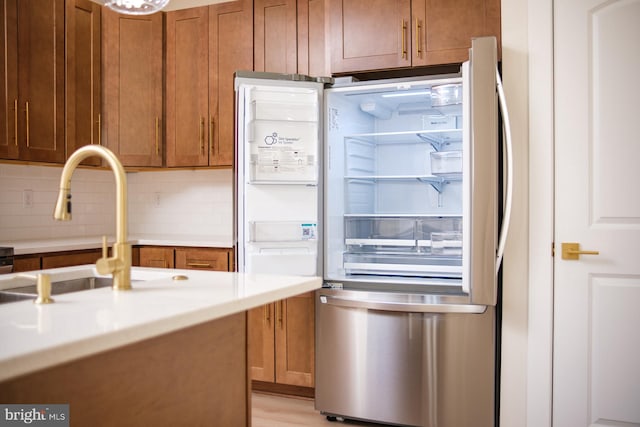 kitchen with brown cabinets, refrigerator with glass door, a sink, light countertops, and decorative backsplash