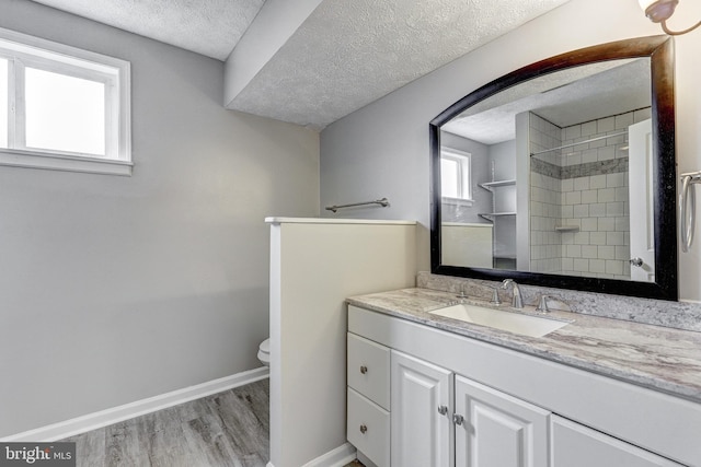 bathroom with baseboards, toilet, vanity, wood finished floors, and a textured ceiling