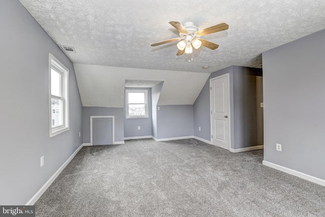 bonus room featuring lofted ceiling, a textured ceiling, carpet floors, baseboards, and ceiling fan