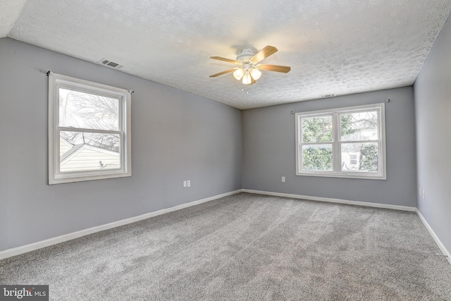 carpeted empty room featuring a textured ceiling, visible vents, baseboards, and ceiling fan