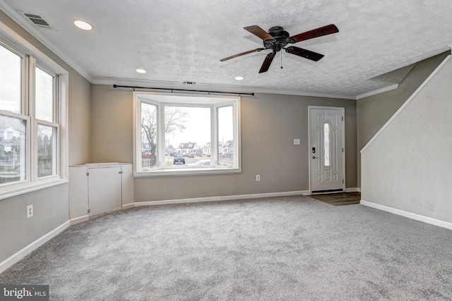 unfurnished living room featuring visible vents, baseboards, carpet, ornamental molding, and a textured ceiling