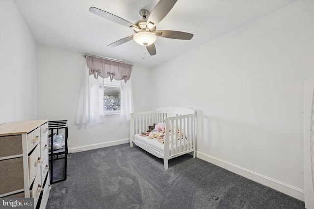 unfurnished bedroom with a ceiling fan, a nursery area, baseboards, and dark colored carpet