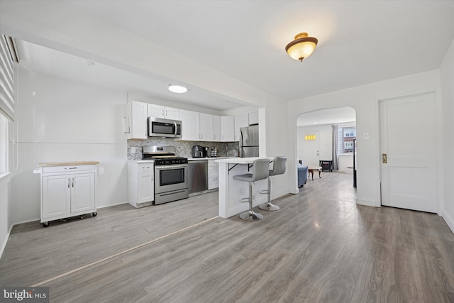 kitchen with white cabinetry, stainless steel appliances, arched walkways, a breakfast bar area, and light countertops