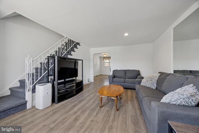 living room featuring recessed lighting, arched walkways, wood finished floors, and stairs