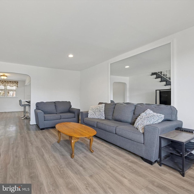 living area featuring arched walkways, recessed lighting, light wood-style flooring, and stairs