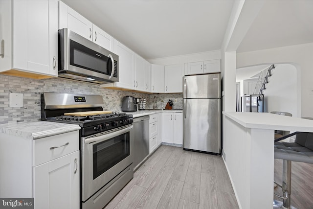 kitchen featuring a breakfast bar, light wood-style flooring, light countertops, appliances with stainless steel finishes, and backsplash