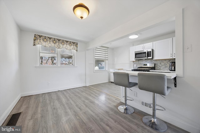 kitchen with visible vents, light countertops, appliances with stainless steel finishes, a kitchen bar, and tasteful backsplash