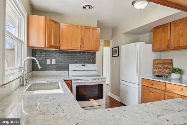 kitchen featuring visible vents, backsplash, light stone counters, white appliances, and a sink