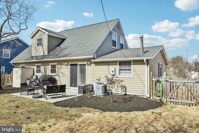 rear view of property with a shingled roof, fence, central AC, a yard, and a patio