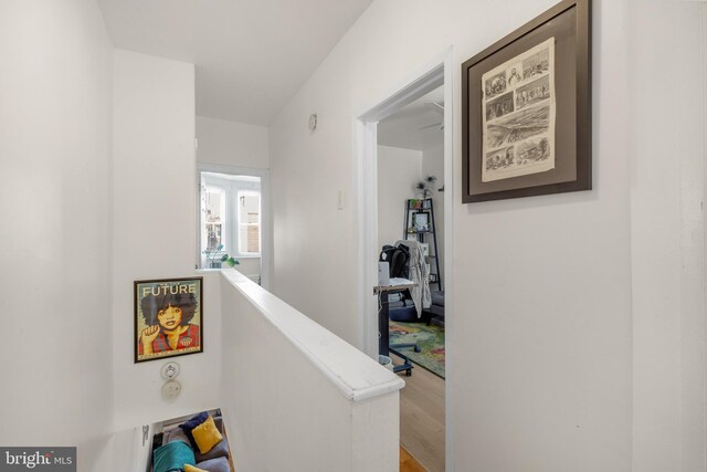hall with wood finished floors and an upstairs landing