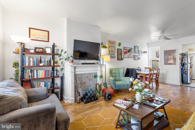 living area with baseboards, a ceiling fan, wood finished floors, and a fireplace