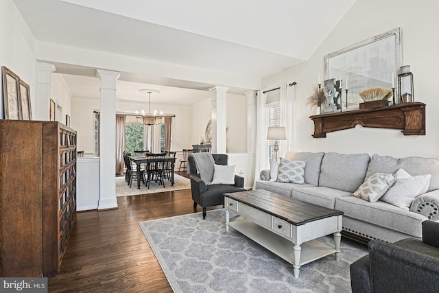 living room featuring a notable chandelier, vaulted ceiling, dark wood-style flooring, and ornate columns