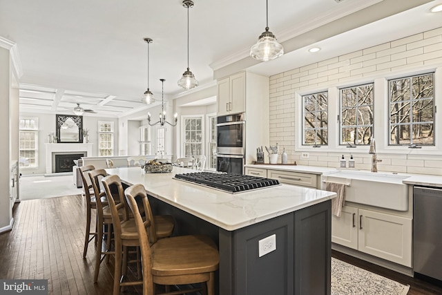 kitchen with a sink, coffered ceiling, a glass covered fireplace, appliances with stainless steel finishes, and decorative backsplash