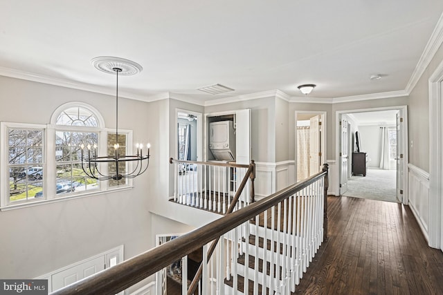 hallway featuring visible vents, dark wood-type flooring, a chandelier, ornamental molding, and an upstairs landing