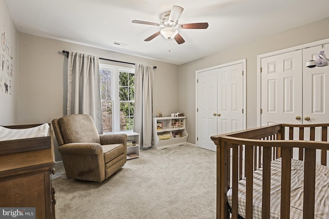 bedroom with a ceiling fan, baseboards, visible vents, light carpet, and two closets