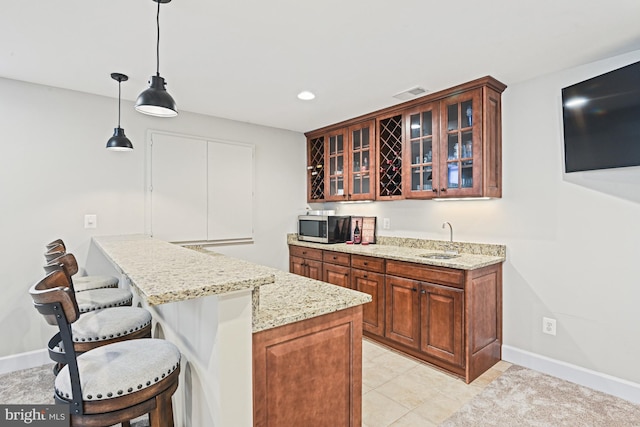 kitchen with visible vents, a sink, glass insert cabinets, a kitchen bar, and stainless steel microwave