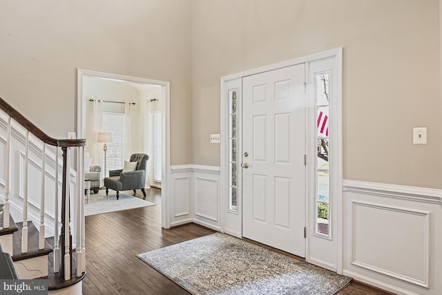 foyer entrance with dark wood-style floors, a decorative wall, wainscoting, and stairs