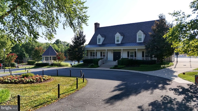 cape cod home featuring fence, aphalt driveway, a front yard, covered porch, and metal roof