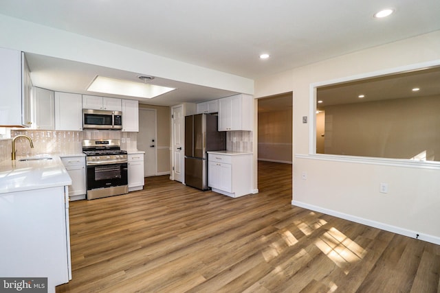 kitchen with a sink, appliances with stainless steel finishes, white cabinets, light countertops, and decorative backsplash