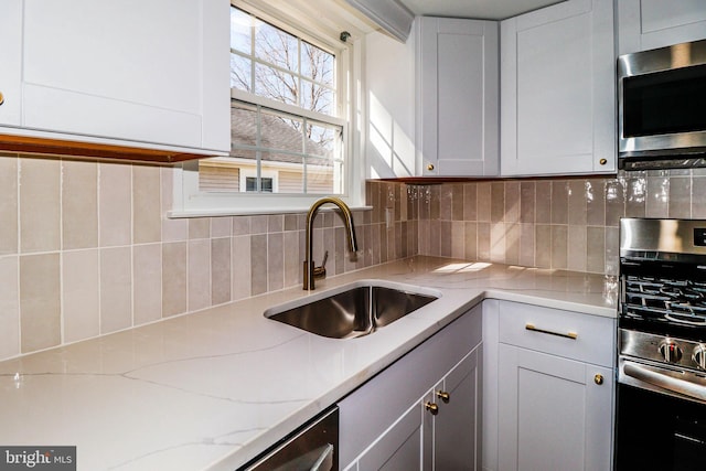 kitchen featuring a sink, stainless steel microwave, backsplash, white cabinets, and light stone countertops