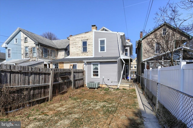 rear view of property with cooling unit, a fenced backyard, and a chimney