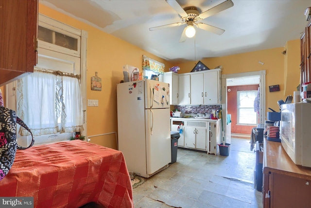 kitchen with decorative backsplash, white cabinetry, freestanding refrigerator, and a ceiling fan