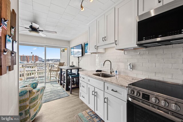 kitchen with light wood-type flooring, decorative backsplash, stainless steel appliances, white cabinetry, and a sink