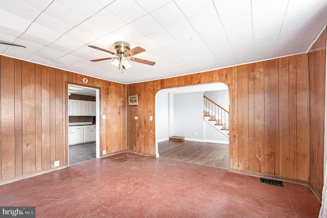 unfurnished room with visible vents, wooden walls, stairs, arched walkways, and a ceiling fan