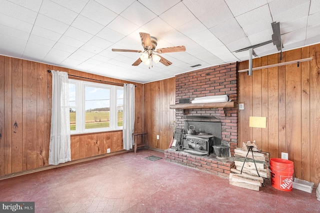 unfurnished living room with visible vents, wood walls, a wood stove, and ceiling fan