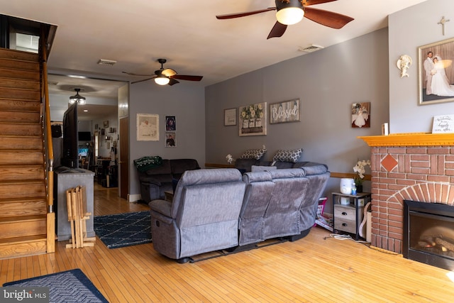 living area with hardwood / wood-style floors, a brick fireplace, ceiling fan, and stairs