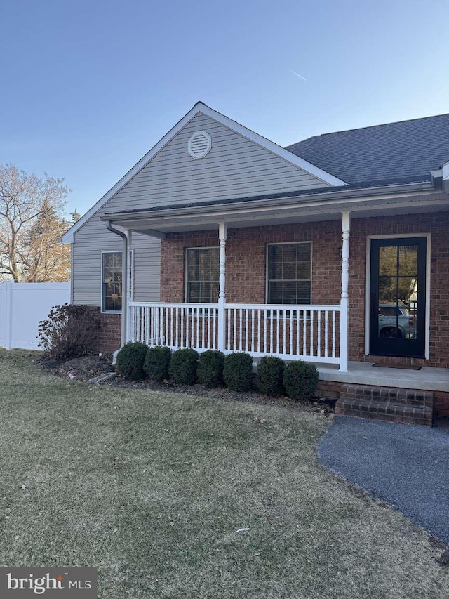 view of front facade featuring brick siding, fence, a porch, roof with shingles, and a front yard