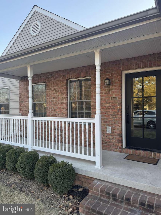 view of exterior entry featuring brick siding and a porch