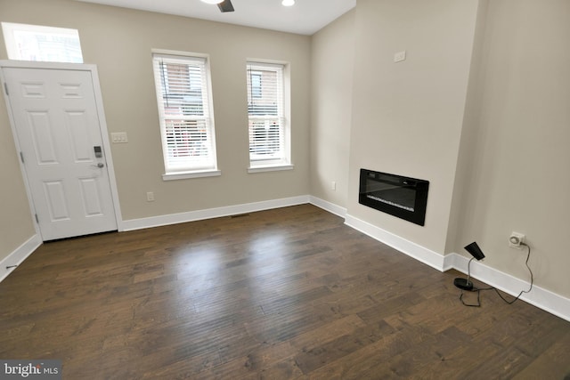 unfurnished living room with a glass covered fireplace, dark wood finished floors, recessed lighting, baseboards, and ceiling fan