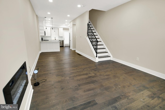 unfurnished living room featuring recessed lighting, stairs, baseboards, and dark wood-style flooring