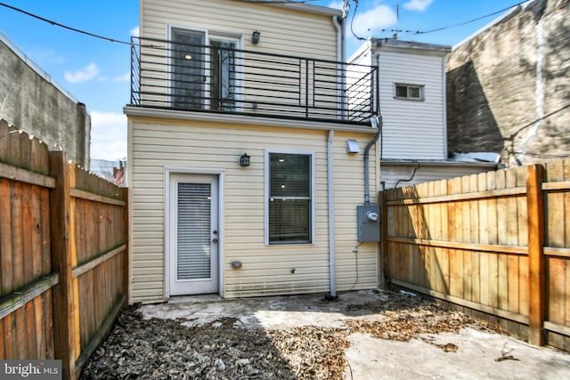 rear view of property featuring a balcony and a fenced backyard