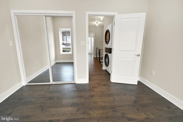 unfurnished bedroom with dark wood-style floors, stacked washer / drying machine, and baseboards