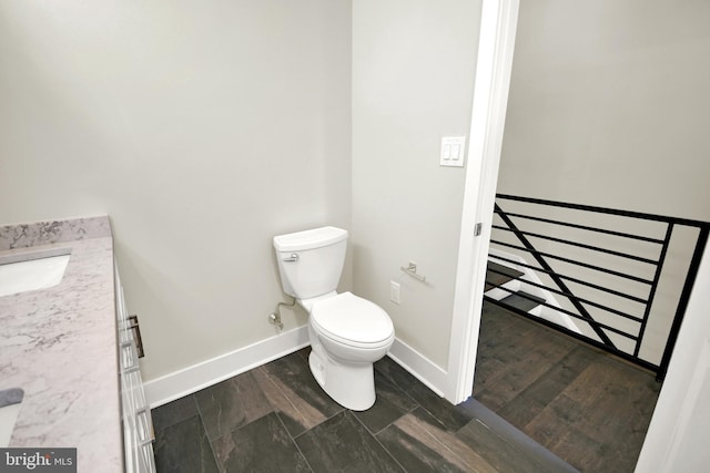 half bathroom with vanity, toilet, wood finished floors, and baseboards