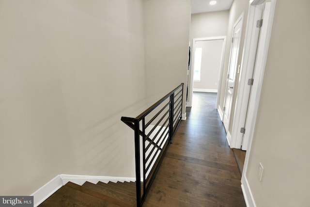 hallway featuring an upstairs landing, baseboards, and dark wood-style flooring