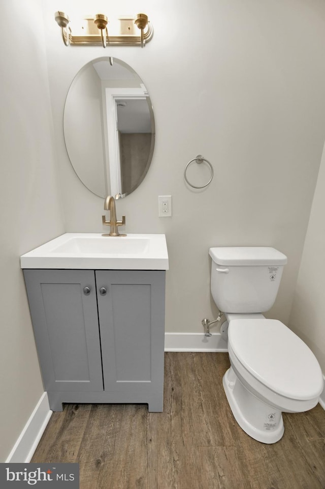 bathroom with toilet, vanity, baseboards, and wood finished floors