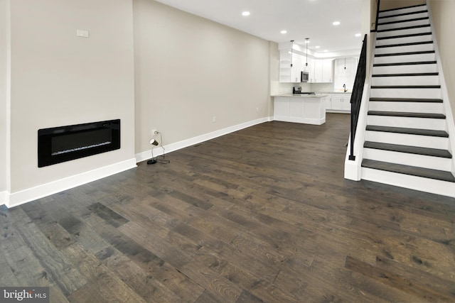 unfurnished living room featuring stairway, baseboards, recessed lighting, dark wood-style flooring, and a glass covered fireplace