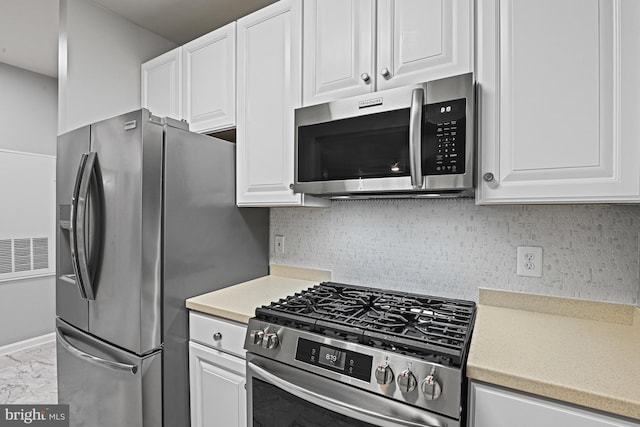 kitchen featuring marble finish floor, backsplash, stainless steel appliances, white cabinets, and light countertops