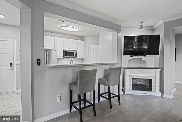 kitchen with baseboards, stainless steel appliances, white cabinets, crown molding, and a kitchen breakfast bar