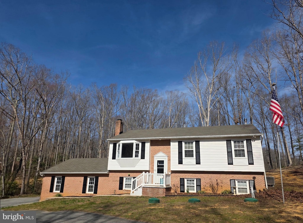 bi-level home with a front lawn, brick siding, and a chimney