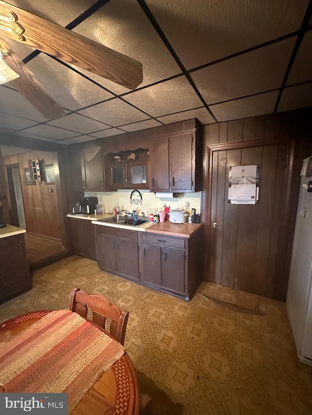 kitchen featuring dark brown cabinetry, a drop ceiling, light countertops, and a sink