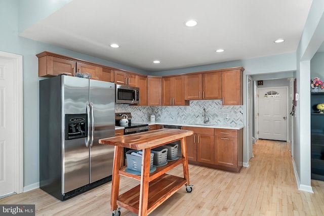 kitchen featuring a sink, light countertops, light wood-style floors, appliances with stainless steel finishes, and tasteful backsplash