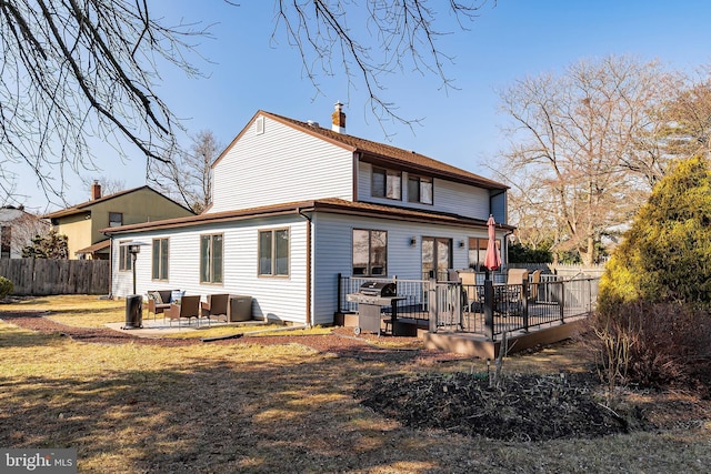 rear view of property featuring a patio, fence, a wooden deck, a yard, and a chimney