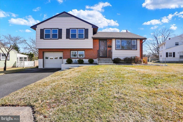 tri-level home featuring a front lawn, aphalt driveway, fence, a garage, and brick siding