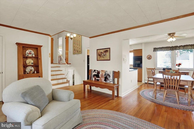 living area with stairs, crown molding, ceiling fan with notable chandelier, and light wood-style floors