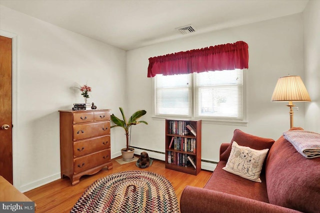 living area featuring light wood finished floors, visible vents, and a baseboard heating unit