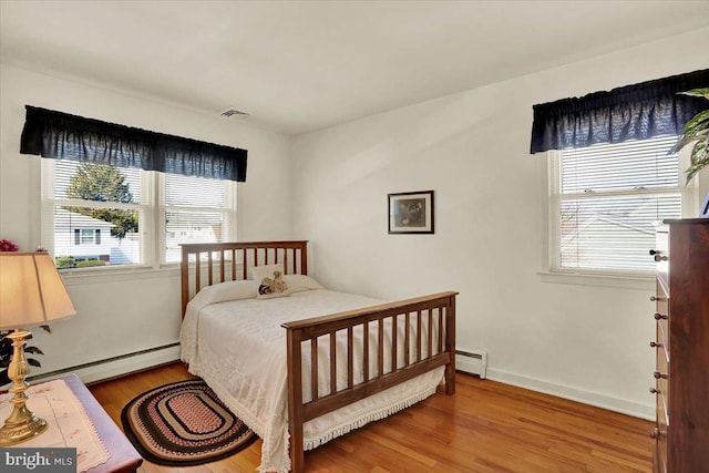 bedroom with visible vents, baseboards, baseboard heating, and wood finished floors